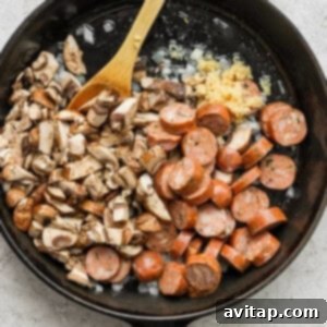 Chicken sausage and mushrooms cooking in a skillet with a wooden spoon.