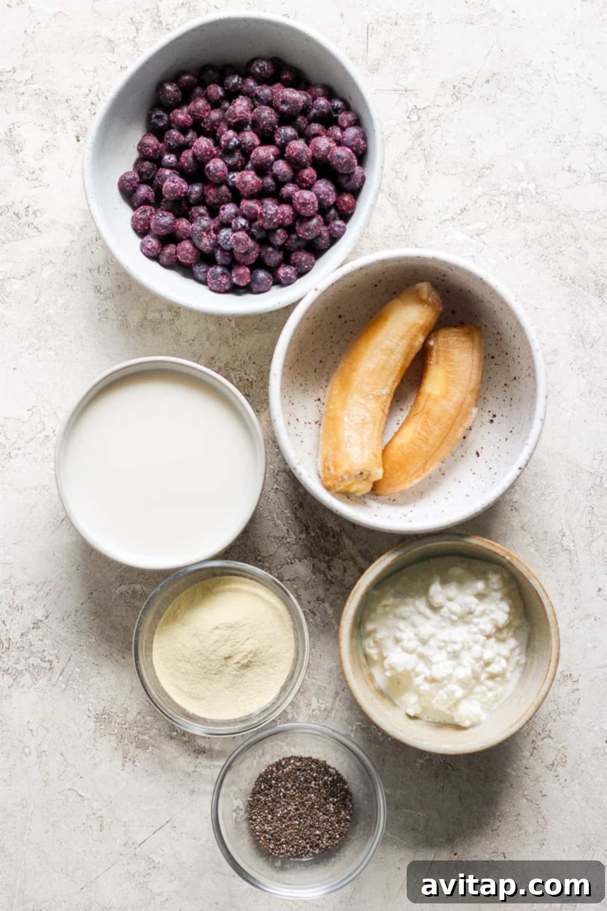 Pouring a fresh blueberry smoothie into a glass jar, surrounded by scattered blueberries on a wooden board.