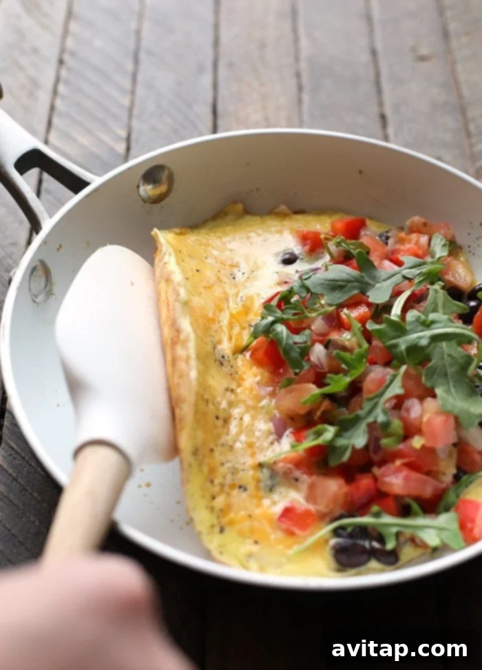 A skilled hand gently folding a vibrant veggie omelette in a hot skillet, showcasing the cooking process.