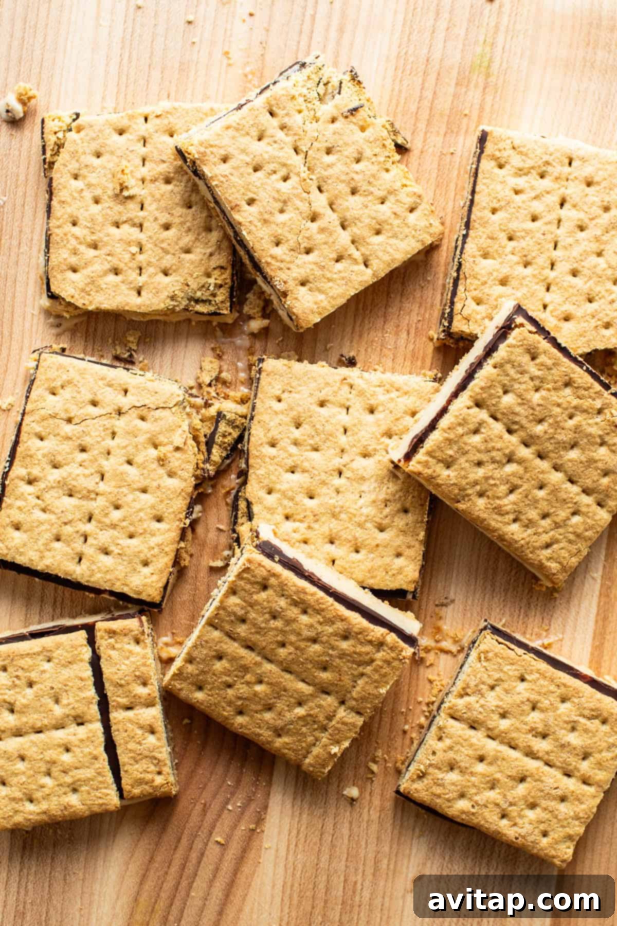 Smores bars with a gooey chocolate filling, scattered on a wooden surface.