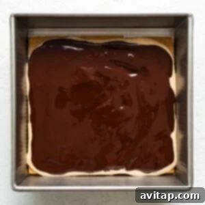 A square baking dish containing a layer of brownie topped with a glossy layer of chocolate ganache.