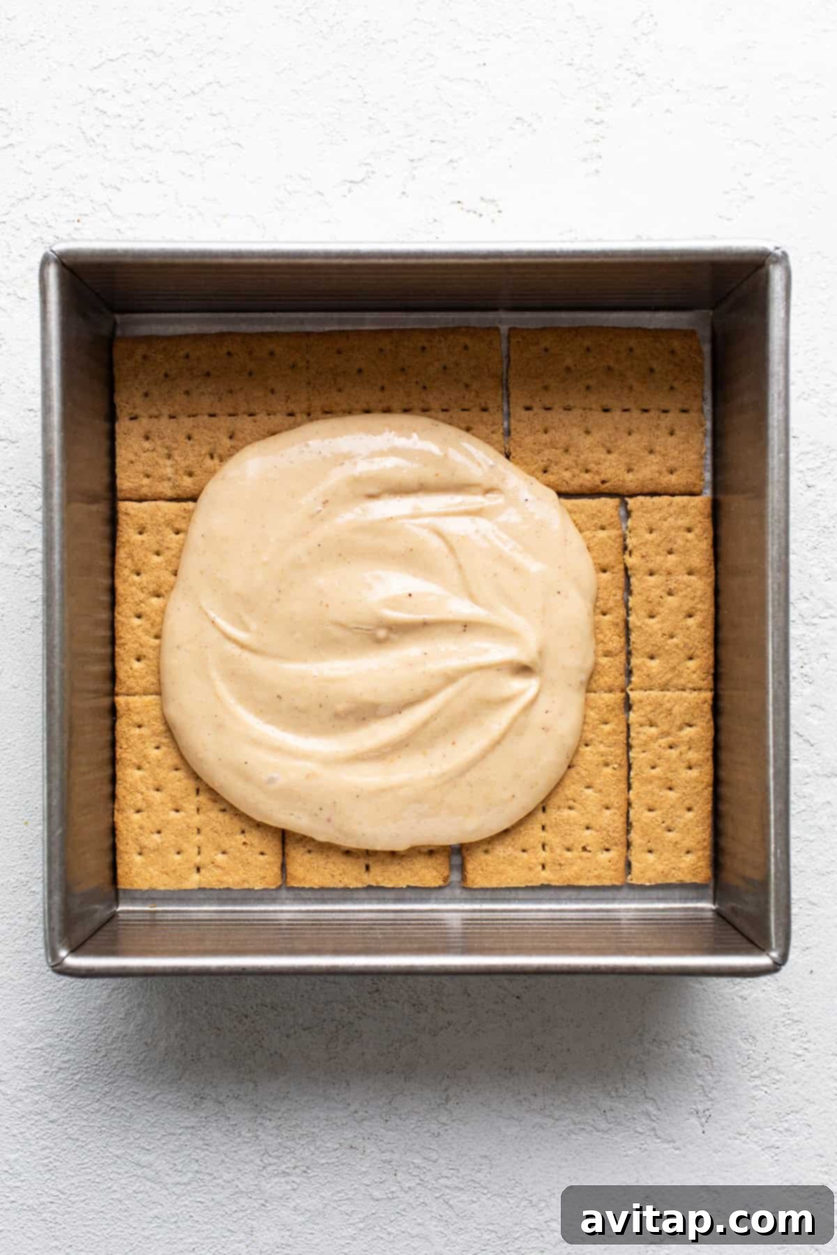 A square baking dish filled with graham crackers topped with a layer of smooth, creamy filling.