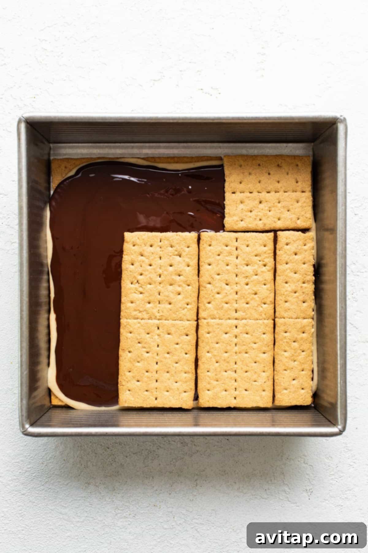 A baking dish with a layer of chocolate topped by aligned graham crackers, preparing for a s'mores dessert.