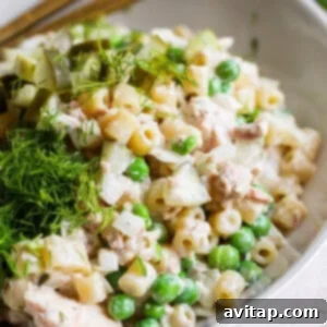 A bowl of pasta salad with peas, diced pickles, chunks of chicken, and fresh dill on top.