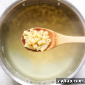 A wooden spoon holding macaroni noodles over a pot of boiling water.