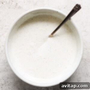 A person mixing ingredients for a creamy sauce in a bowl with a whisk.