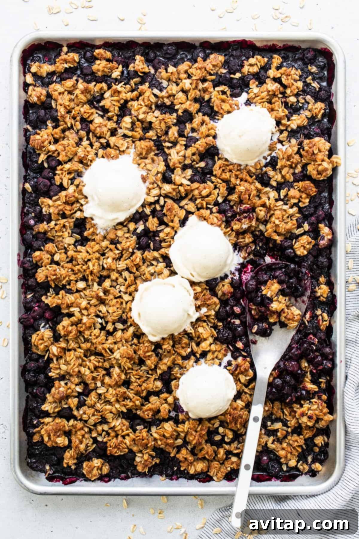 Freshly baked blueberry crumble with scoops of vanilla ice cream on top, ready to be served from a sheet pan.