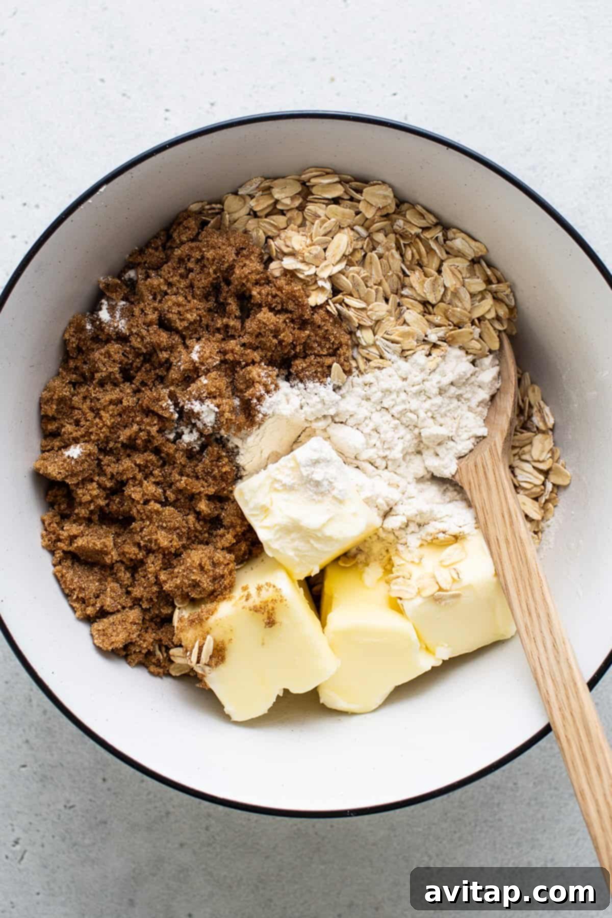A selection of baking ingredients, including oats, flour, and sugar, in a bowl with a wooden spoon, ready for preparing the crisp topping.