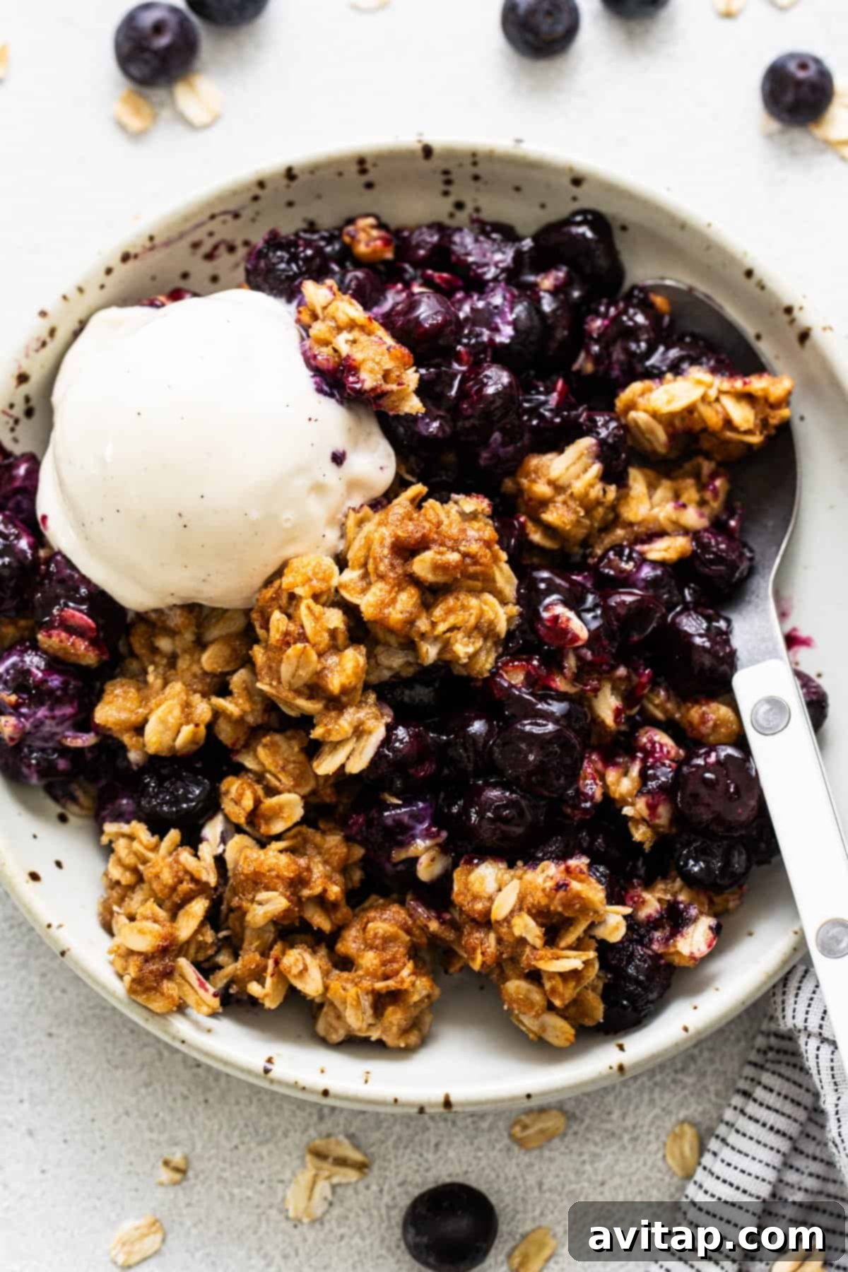 A bowl of blueberry crumble generously topped with a scoop of creamy vanilla ice cream, ready to be enjoyed.