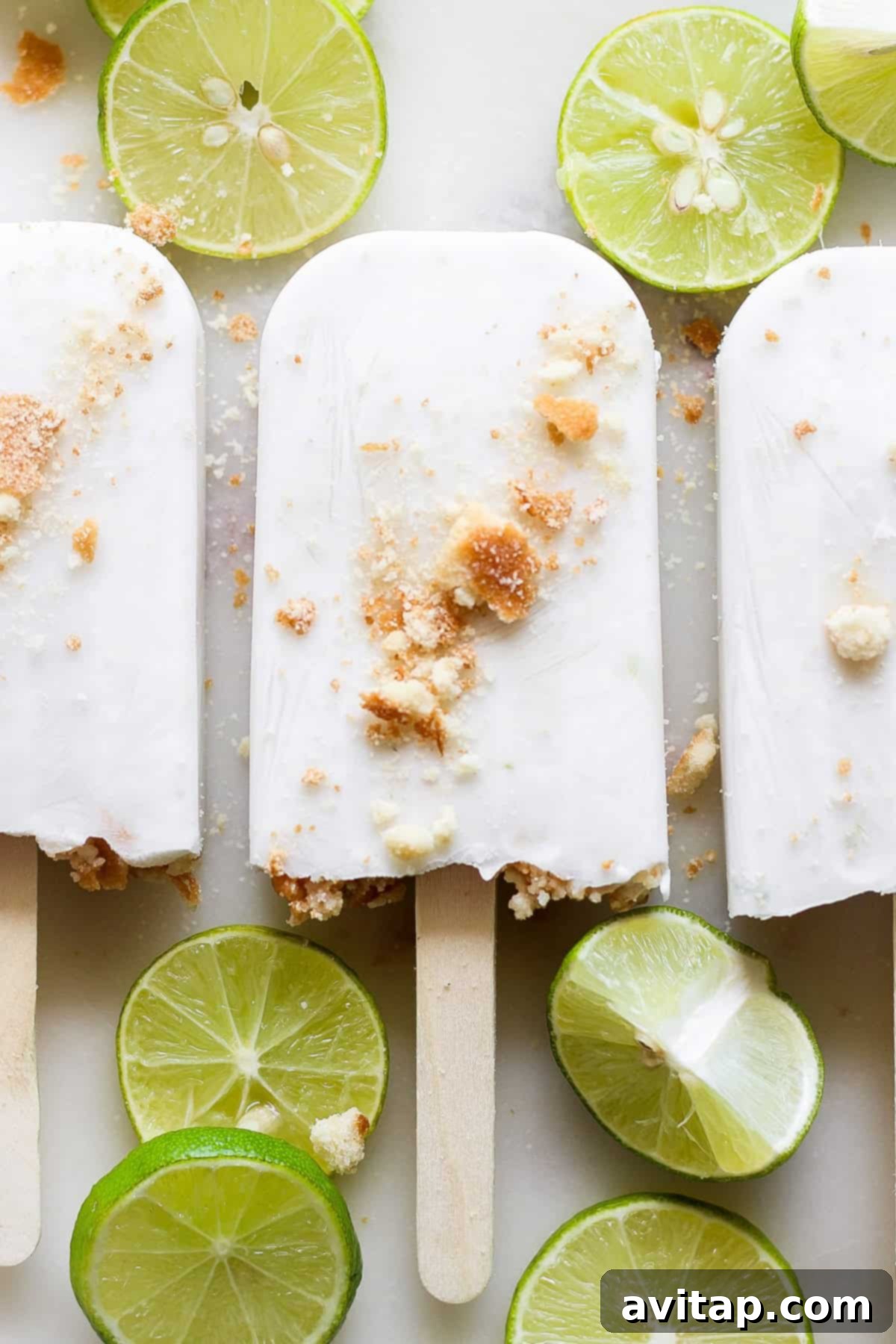 Two Coconut Key Lime Pie Popsicles on a white background, garnished with lime zest and coconut flakes.