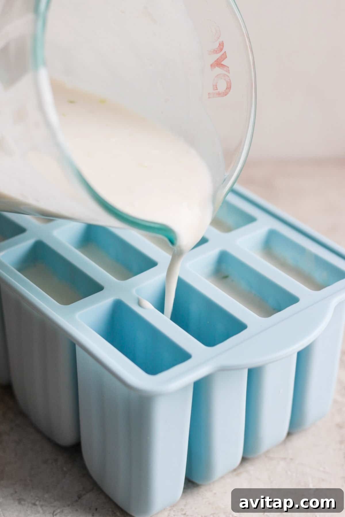 Close-up of a Coconut Key Lime Pie Popsicle mixture being poured into molds.