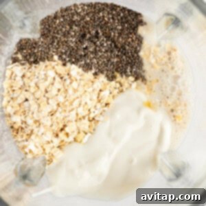 Ingredients including chia seeds, oats, and a creamy liquid mixture in a blender container, viewed from above, ready to be blended.