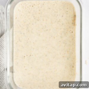 A glass container filled with oatmeal mixture is on a countertop, ready for the next step of the recipe.