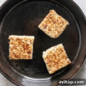 Three toasted Rice Krispie treats in a cast iron skillet on a light textured surface, perfectly golden-brown.