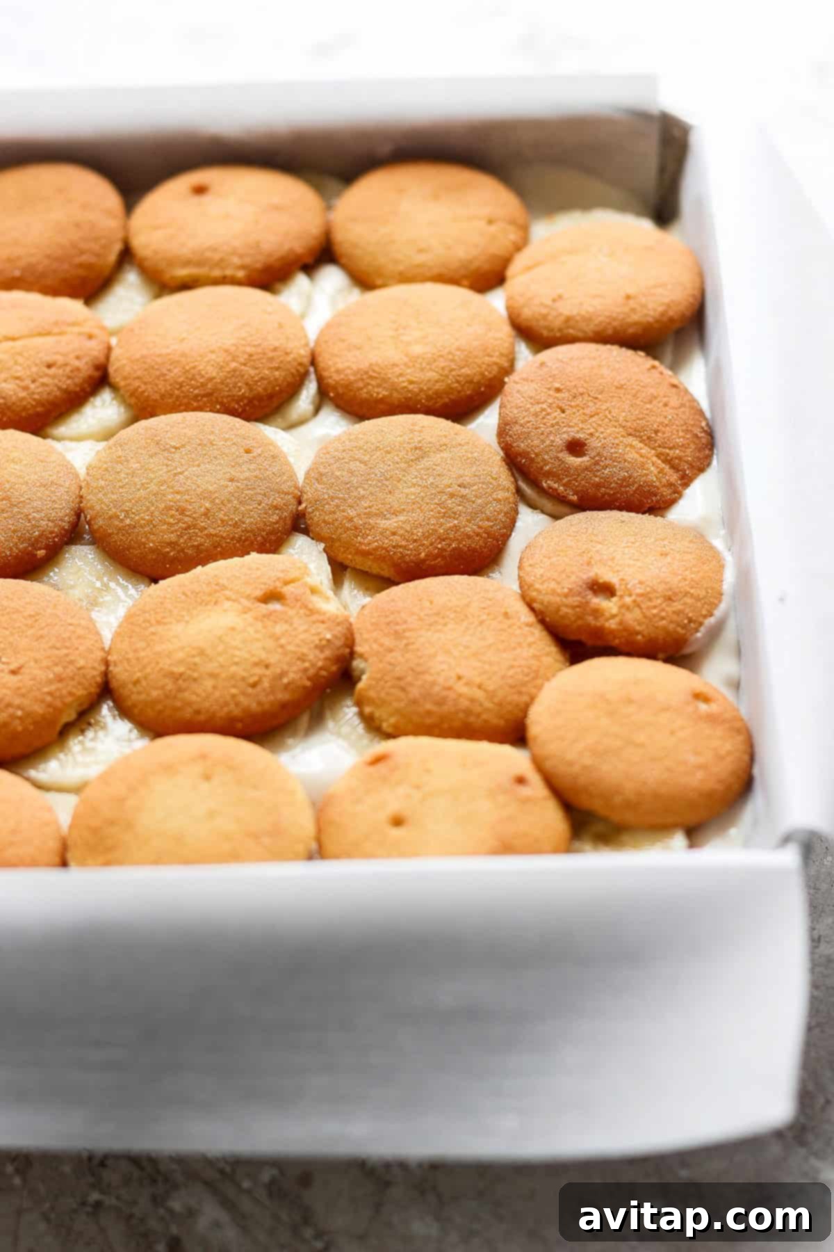 Peanut Butter Banana Icebox Delight 3 A baking dish filled with layers of vanilla wafer cookies, partially submerged in a creamy mixture, transforms into a delectable peanut butter banana ice box cake.