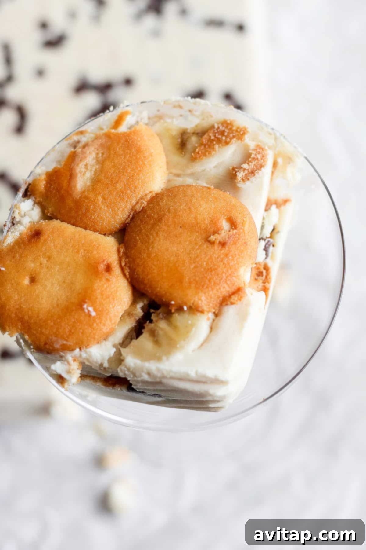 Peanut Butter Banana Icebox Delight 6 A glass bowl filled with a dessert made of layered vanilla wafers, slices of banana, and creamy pudding. The dessert, reminiscent of a peanut butter banana ice box cake, is topped with vanilla wafers.