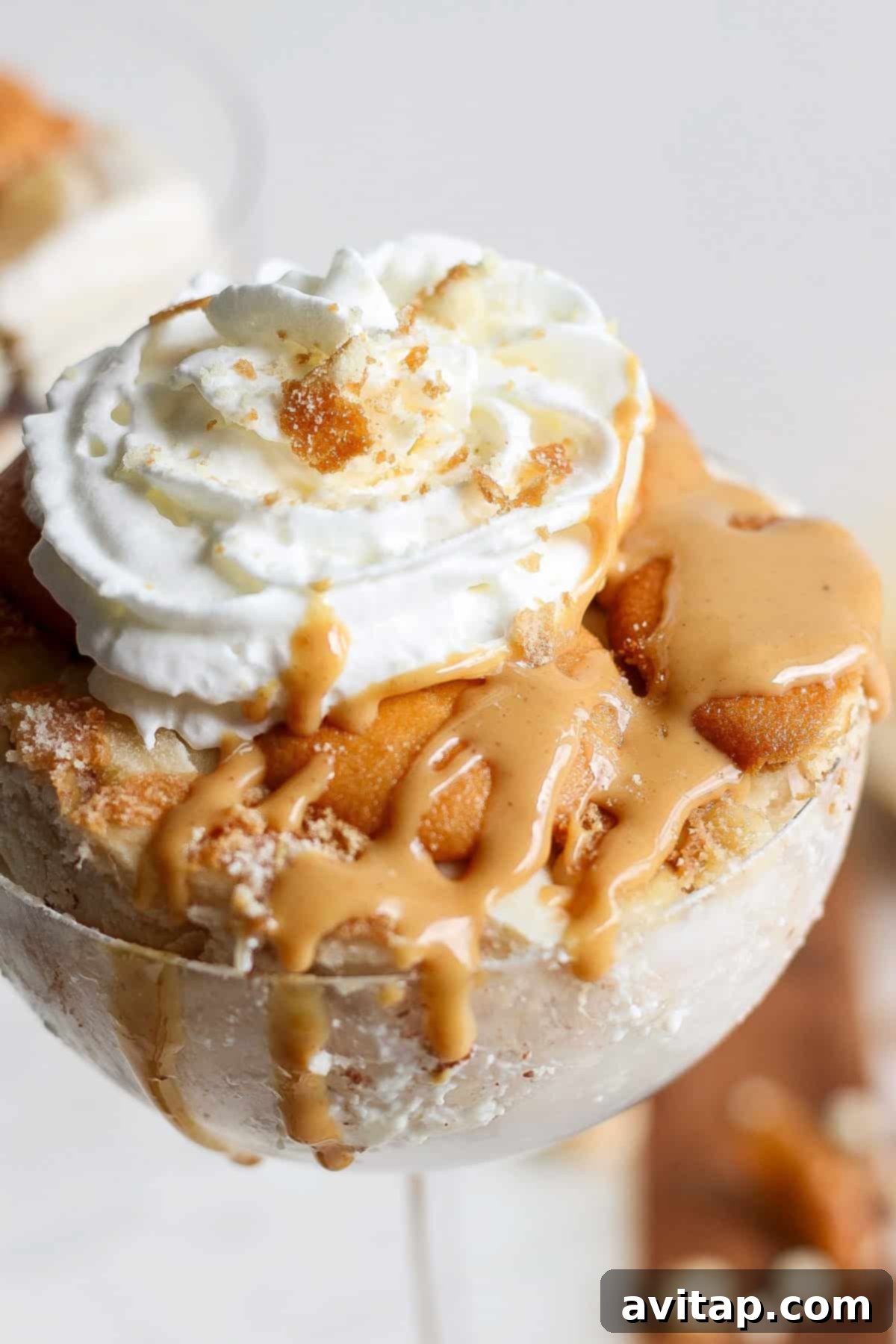 Peanut Butter Banana Icebox Delight 7 Close-up of a peanut butter banana ice box cake topped with whipped cream, caramel sauce, and cookie crumbs, served in a glass container.
