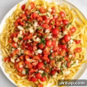 A plate of fettuccine pasta topped with chopped tomatoes, onions, and herbs.