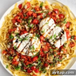 A plate of pasta topped with two poached eggs, cherry tomatoes, herbs, and a drizzle of balsamic glaze.