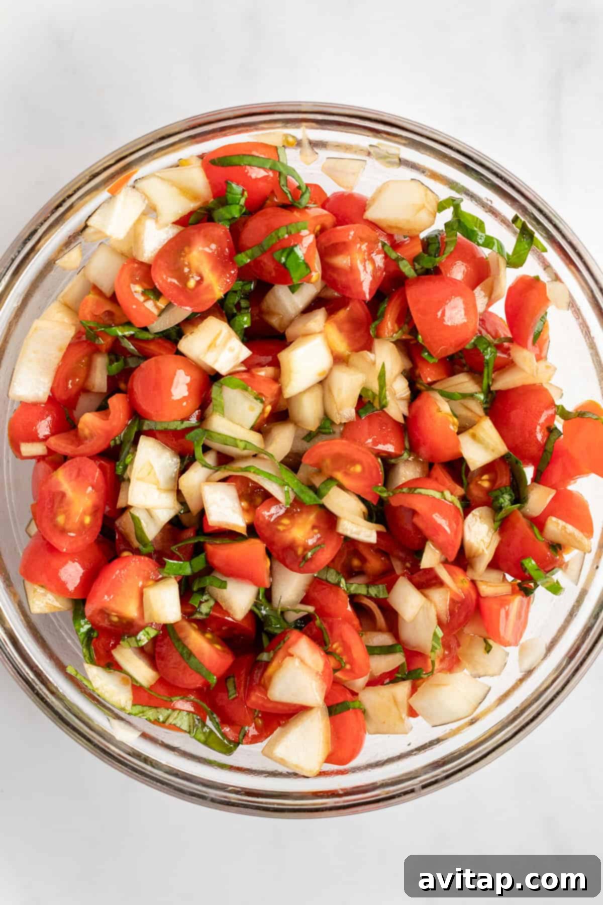 A vibrant glass bowl filled with a fresh bruschetta mixture of chopped tomatoes, onions, and basil, ready to be added to pasta.