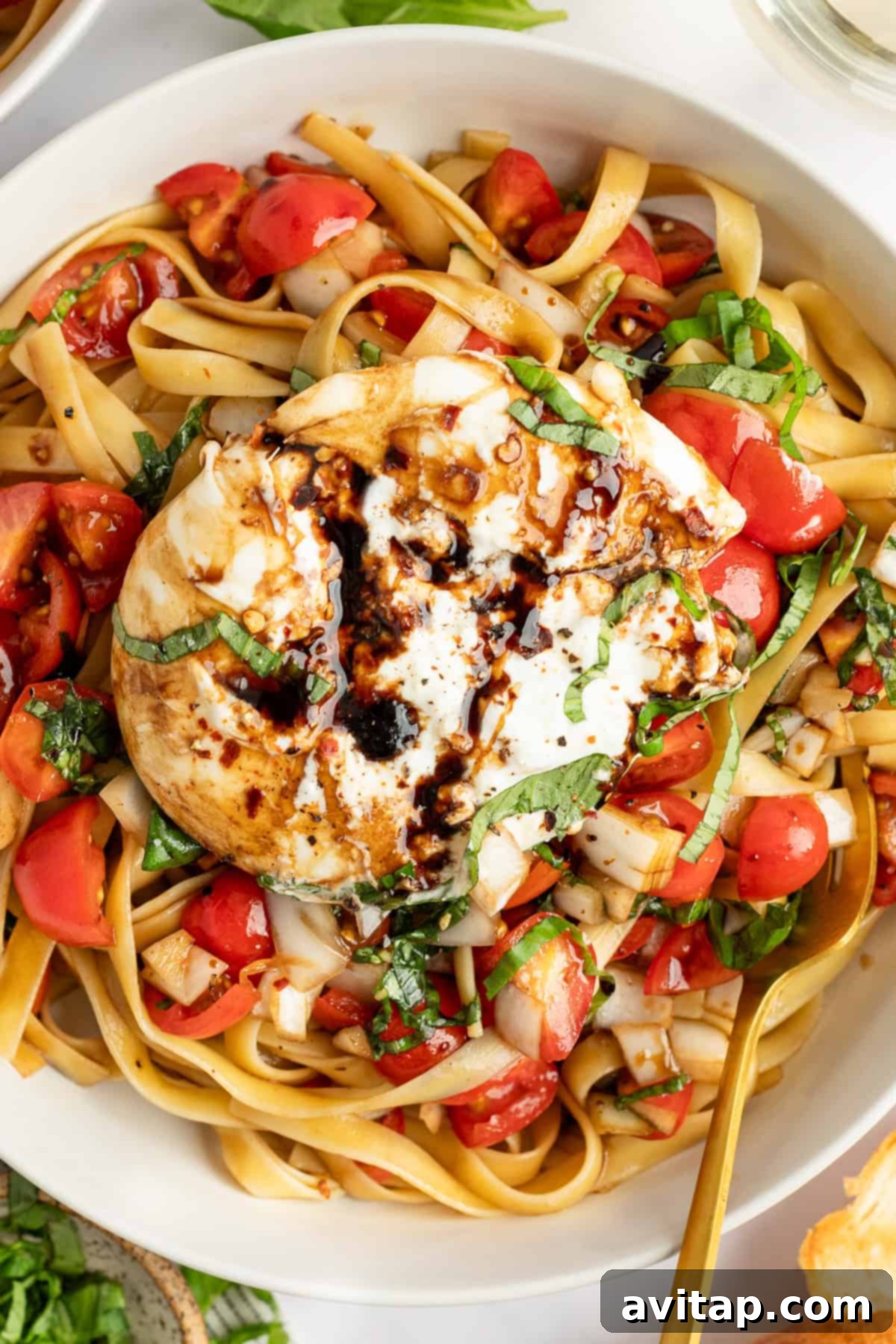 A beautifully composed bowl of bruschetta pasta featuring a whole burrata cheese ball, artfully drizzled with balsamic glaze and garnished with fresh herbs and tomatoes.