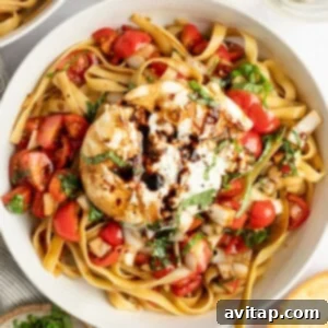 A bowl of pasta with tomatoes, fresh basil, and a large mozzarella ball drizzled with balsamic glaze.