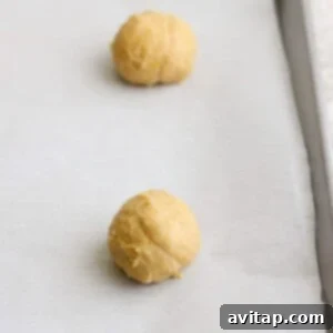 Two balls of lemon cookie dough placed on a parchment-lined baking sheet, destined for a sweet finish with cream cheese frosting.