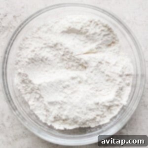 A clear glass bowl filled with white flour rests on a textured gray surface, ready for crafting delicious lemon cookies with cream cheese frosting.