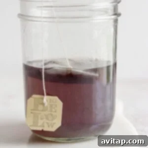 Herbal tea bag steeping in a jar of water, creating a deep purple base for the cocktail.