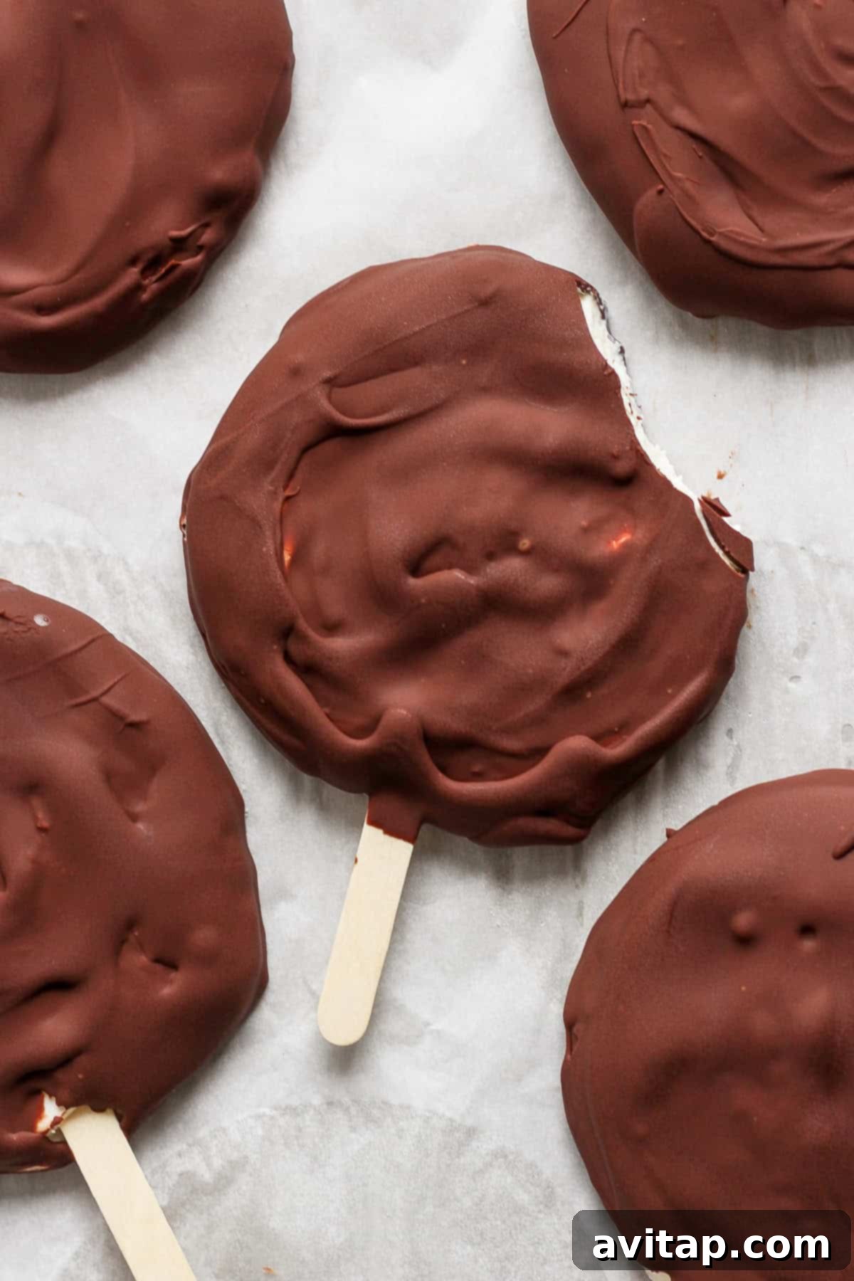 Delicious Homemade Dilly Bars 2 Chocolate-covered ice cream bars on sticks, viewed from above, with one bar having a bite taken out of it.