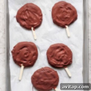 Delicious Homemade Dilly Bars 11 Five chocolate-covered treats on wooden sticks rest on a parchment-lined baking sheet.