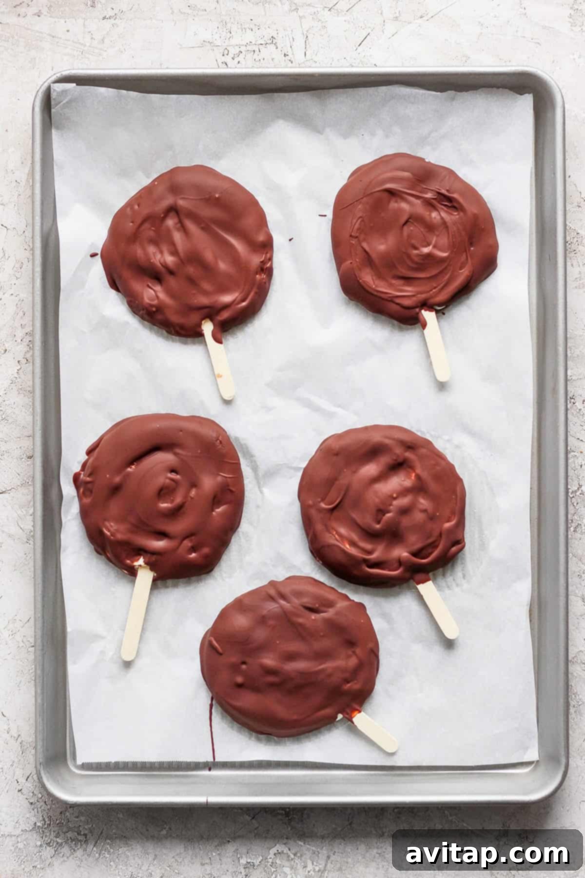 Delicious Homemade Dilly Bars 5 Five chocolate-covered treats on wooden sticks rest on a parchment-lined baking sheet.