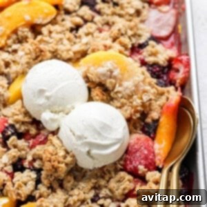 A dessert tray with fruit crisp topped with two scoops of vanilla ice cream and a spoon on the right side.