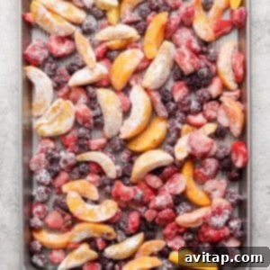 A baking sheet filled with an assortment of frozen fruit slices including peaches, strawberries, and blackberries arranged evenly across the surface.