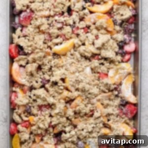 A baking tray filled with a mixture of sliced fruits, including peaches and berries, topped with a crumbly oat mixture, ready to be baked.