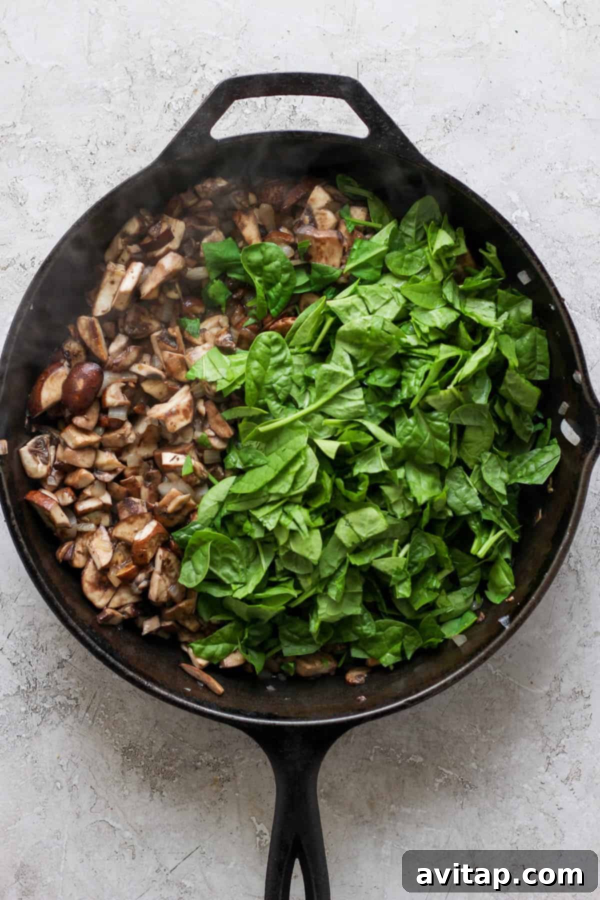 Artisan Pesto Lasagna 3 A rustic cast-iron skillet divided, with chopped Bella mushrooms on one side and fresh, vibrant green spinach on the other, prepared for sautéing.