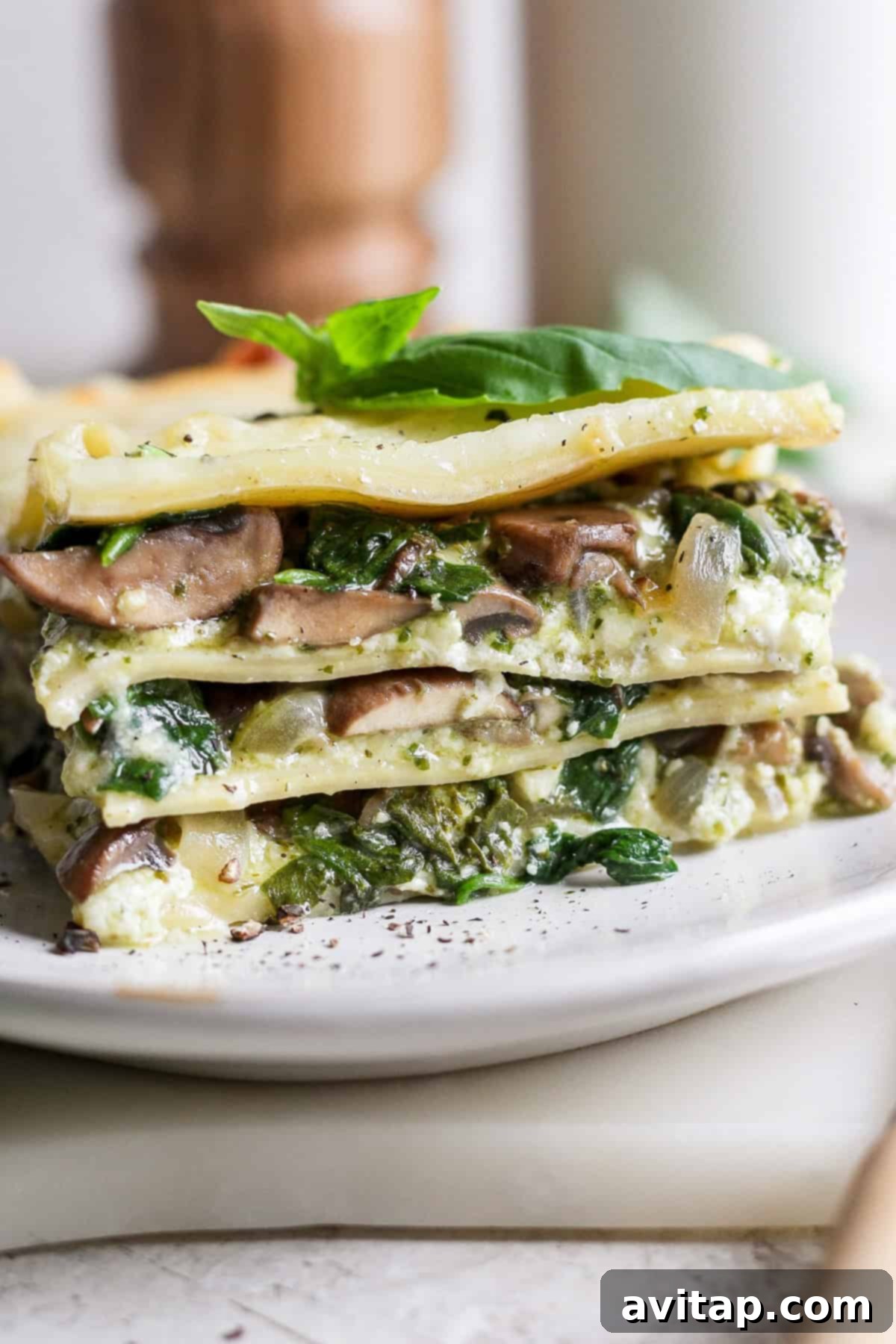 Artisan Pesto Lasagna 8 A single, perfectly plated slice of vibrant green vegetable pesto lasagna, garnished with a fresh basil leaf, showcasing its distinct layers of pasta, mushrooms, spinach, and creamy cheese.