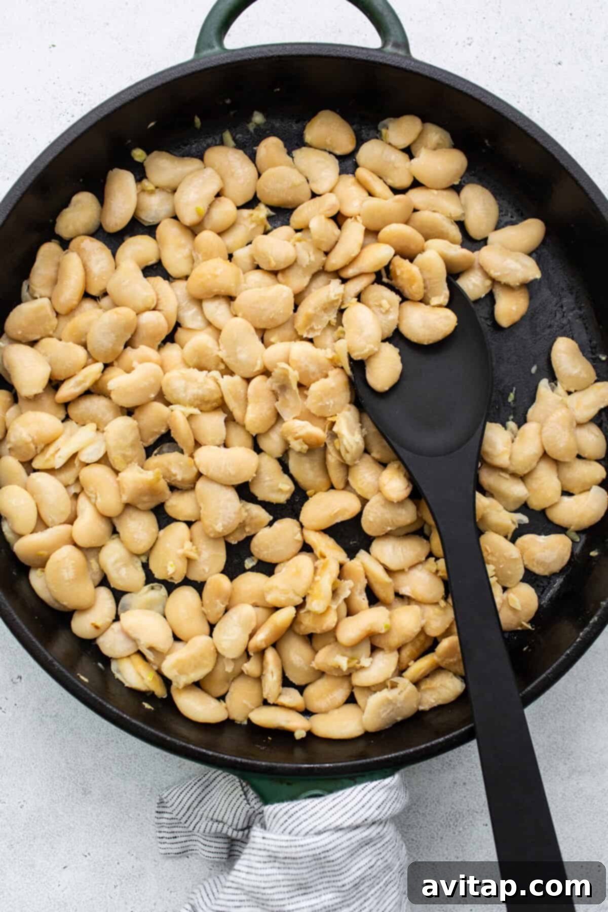 Creamy butter beans gently sautéing in a skillet, absorbing the aromatic flavors of garlic and olive oil.