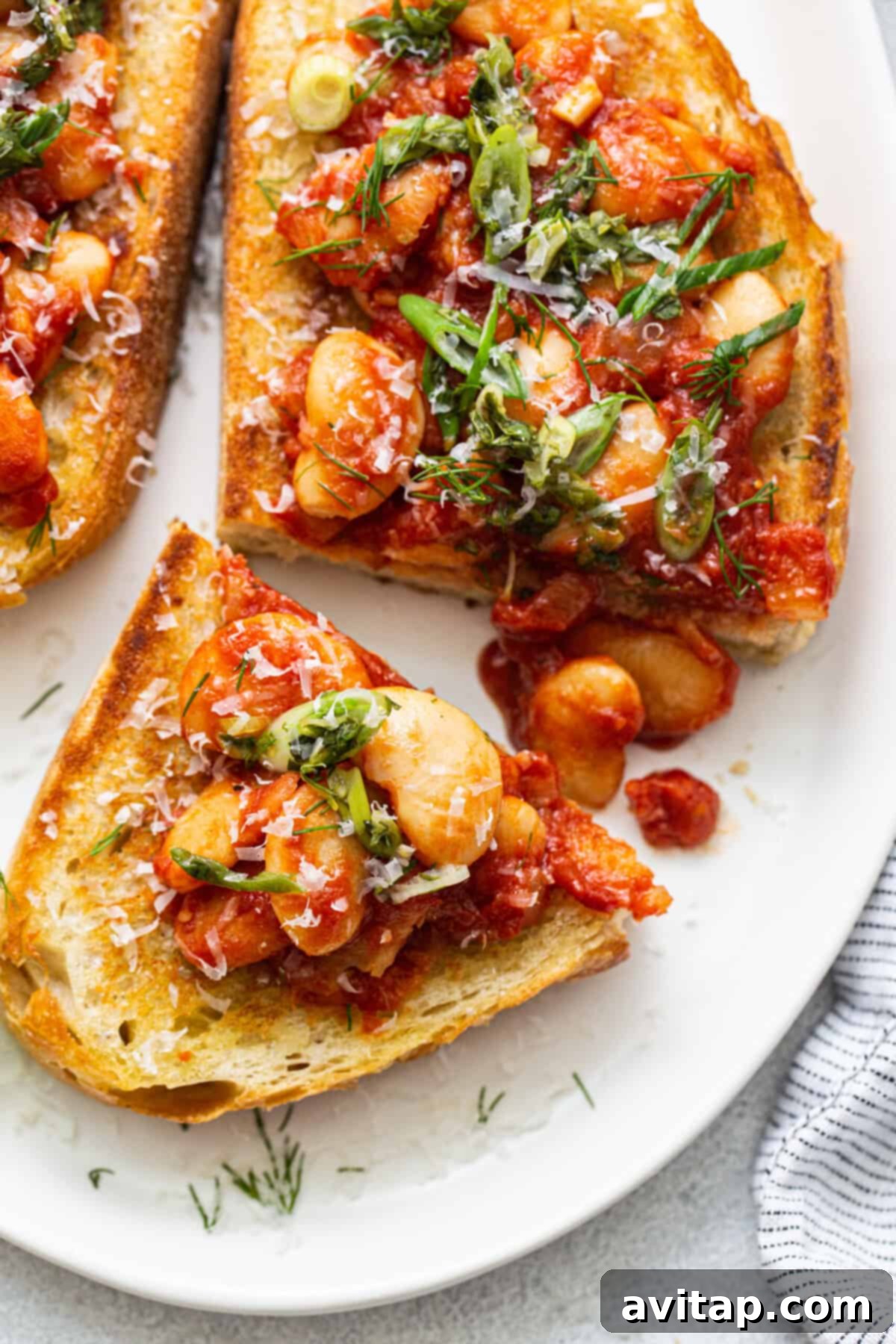 Two perfectly arranged slices of toasted bread, topped with the rich butter bean and tomato mixture, elegantly garnished with fresh herbs and a sprinkle of Parmesan cheese.