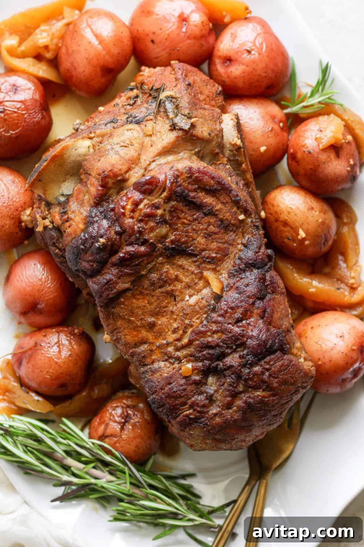A beautifully roasted pork shoulder with a crispy, golden-brown exterior, surrounded by perfectly browned red potatoes and fresh sprigs of rosemary, elegantly arranged on a pristine white serving platter.