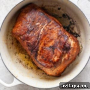 A cooked, browned piece of meat in a white pot, showing seared and crispy edges.