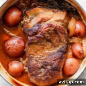 A cooked pot roast with potatoes and onions in a white enameled cast iron pot.
