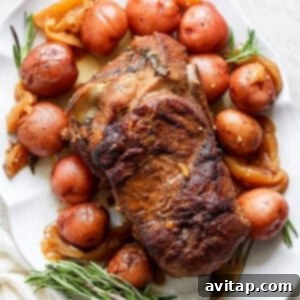 An oven-roasted pork roast surrounded by red potatoes and garnished with rosemary on a white platter.