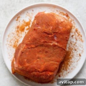 A piece of seasoned raw meat on a white plate, placed on a textured white surface.