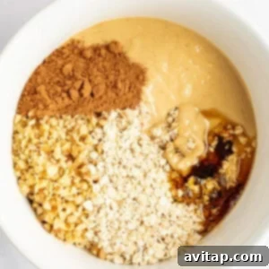 A large white mixing bowl containing the perfectly combined ingredients for the oat layer: peanut butter, chopped nuts, quick-cooking oats, cocoa powder, and a drizzle of honey, all stirred together to form a rich, textured mixture ready for shaping.