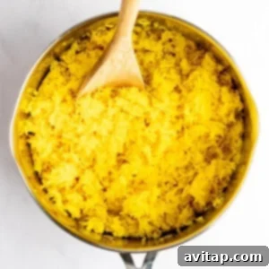 A saucepan filled with yellow rice and a wooden spoon resting inside.