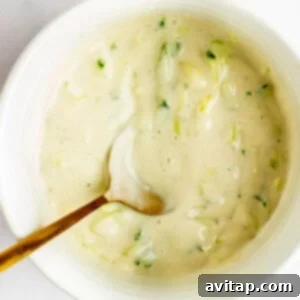 A bowl of creamy dressing with chopped green herbs and a spoon inside.