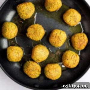 A skillet with twelve golden-brown falafel balls frying in oil on a light-colored surface.