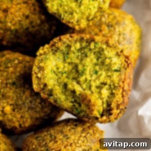 Close-up of a halved falafel, revealing its green, crispy interior. Other whole falafel pieces arrange in the background on parchment paper.