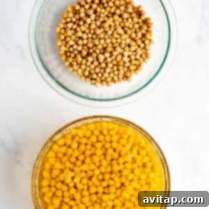 Two glass bowls on a marble surface: one with dried chickpeas and the other with soaked chickpeas in water.